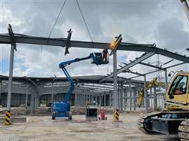 A worker in an aerial platform torch cuts steel at height