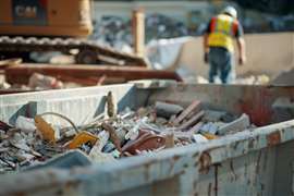 Large rolloff dumpster with assorted construction waste, worker in background