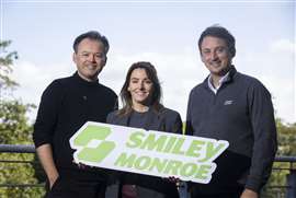 Smiley Monroe's new brand logo cut-out being held be three members of its team.